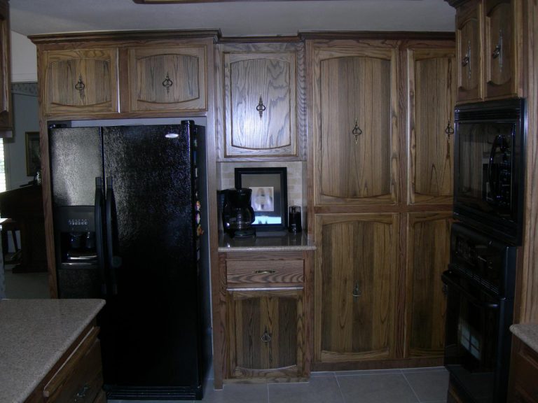 A kitchen with wooden cabinets and a black refrigerator.