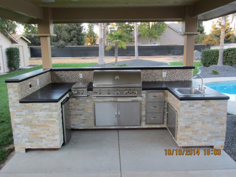 An outdoor kitchen with a grill and sink.