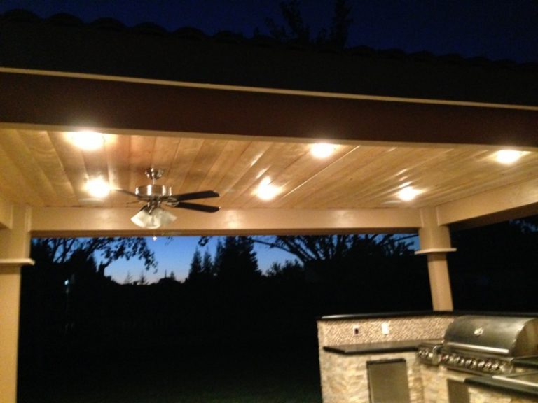 A covered patio with a grill and lights at night.