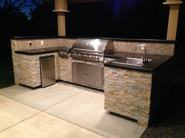 An outdoor kitchen with a grill and sink.