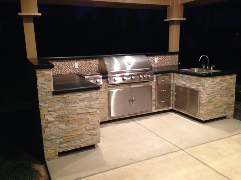 An outdoor kitchen with a grill and sink.