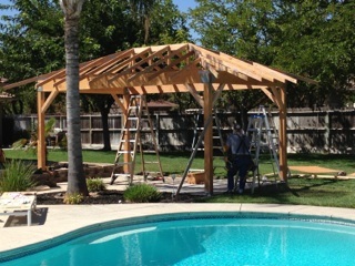 A wooden gazebo is being built in a backyard.