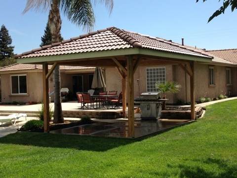 A backyard with a wooden gazebo and a grill.