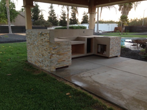 An outdoor kitchen with a stone countertop and a pool.
