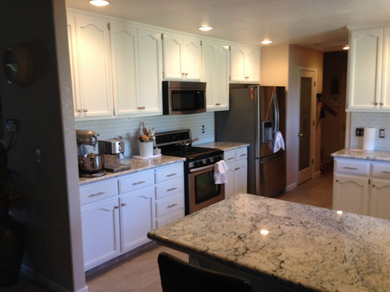 A kitchen with white cabinets and granite counter tops.