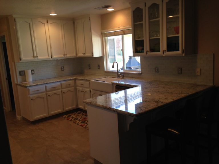 A kitchen with white cabinets and granite counter tops.