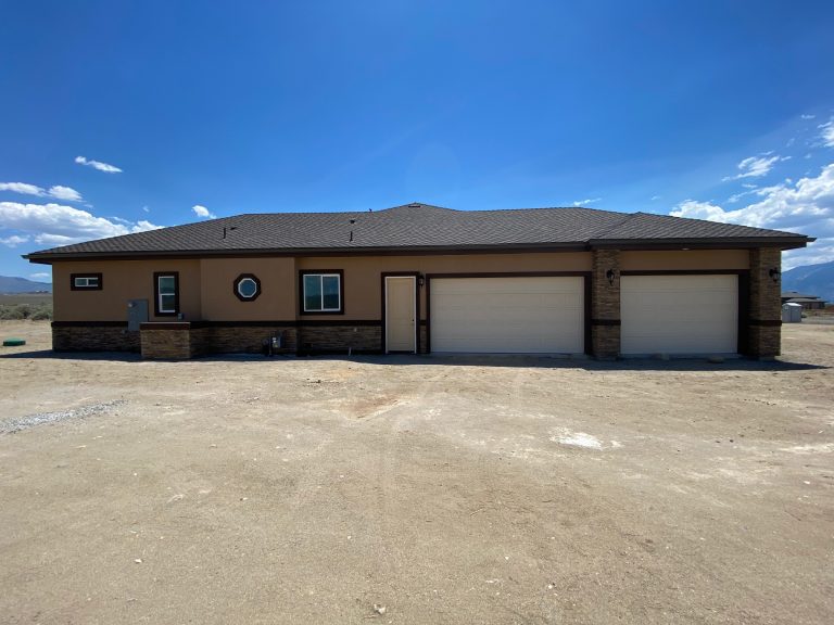 A home with two garages and a dirt driveway.